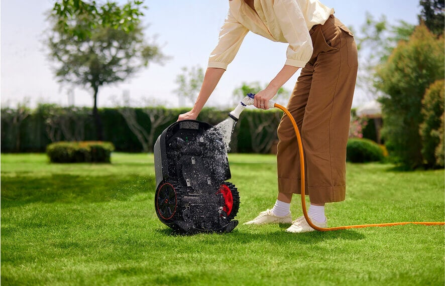 Woman using MoeBot lawn mower on green grass with trees in background